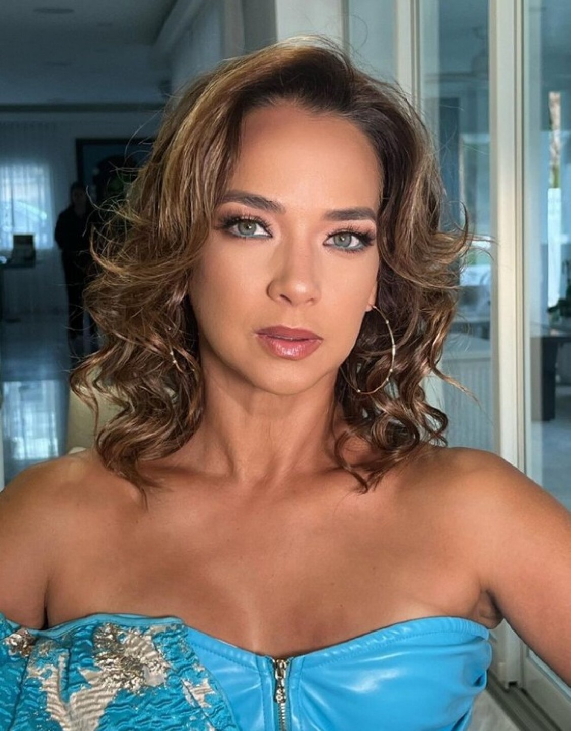 Adamari López posando seriamente para redes sociales vestida de azul con el cabello ondulado